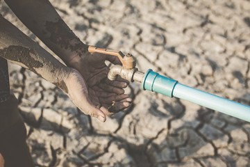 Hand of boy want to drink some water on crack ground , Concept drought and shortage of water crisis