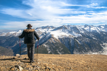 Naklejka premium Słoneczny stok pokryty śniegiem i człowiek wspinający się z kijkami trekkingowymi.