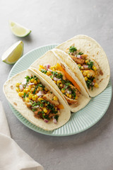 Three mexican tacos with chicken, corn, sweet pepper and parsley in the blue plate on the table.