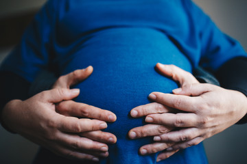 close up of a belly hugged by the hands of parents