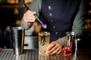 Bartender finishing preparing cocktail with an violet flower