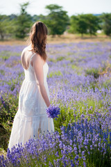 Fototapeta na wymiar young woman in white dress with flower bouquet in hand on lavender field in summer