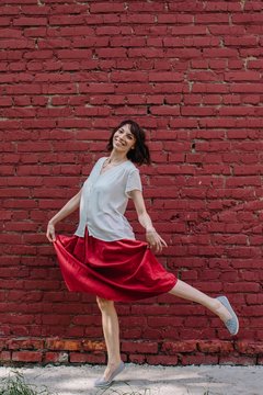 Joyful dancing young female looking at camera and smiling in front of red brick wall