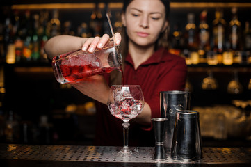 Bartender girl pouring a fresh light red cocktail