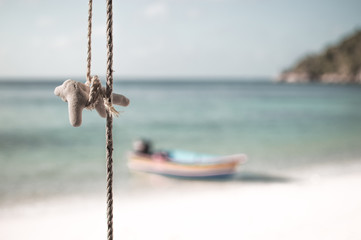 Fototapeta premium A piece of coral hanging from rope in a beach, a small boat by the beach in the background