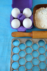 Eggs, flour and kitchen utensils for cooking homemade dumplings on blue background