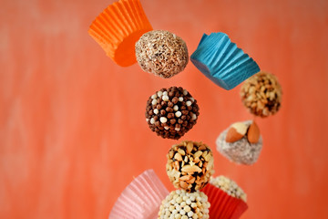 Flying sweets with different sprinkles and paper cups on colourful orange background