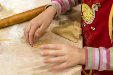 Little girl rolls out the dough. The child makes pastry with dough from forms