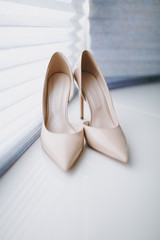 Close up Elegant light beige wedding varnish shoes with thin heels and sharp noses for the bride on a white gloss windowsill background. Wedding wear, accessories