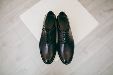 Close up Beautiful elegant wedding polished black shoes with shoelaces for the groom on a chair on background a light wooden floor. Wedding wear, accessories