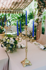 Beautiful and exquisite decoration of the wedding celebration in in the middle of a green garden. Banquet served table with a beige tablecloth, plates and candlesticks with blue candles under cover