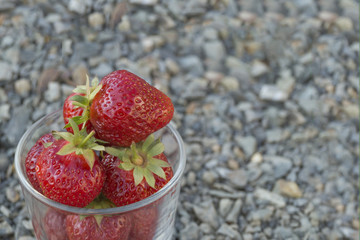 Glass full of red strawberries stands on the grey crushed stones.