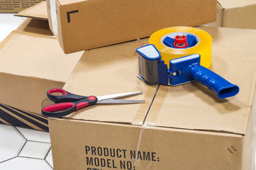 Packing tape dispenser and the scissors on the cardboard box.