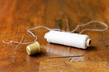 Thimble, a needle and a spool of white thread on an antique wood veneer full of cracks. Selective...