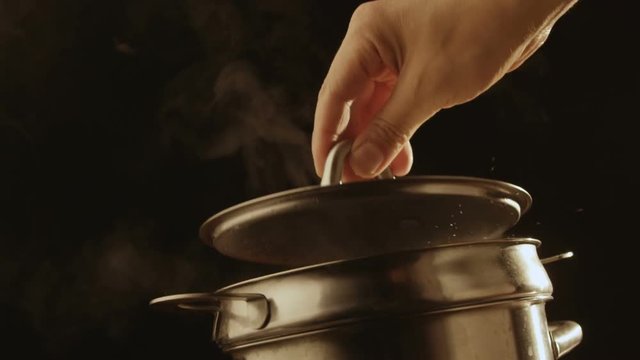 Hand opens the lid of a pot of boiling water