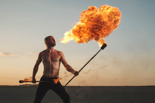 Male acrobat performing spitting fire act at the beach
