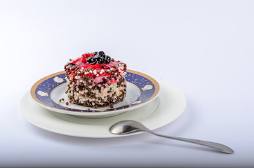 appetizing cake with red jelly on its top and decorated with black currant, sprinkled with rice balls on two saucers white and with a blue stripe on the edge, next is a spoon, place under the text on 