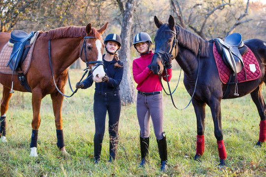 Two teenage girls with their horses in autumn park. Equestrian sport background with copy space