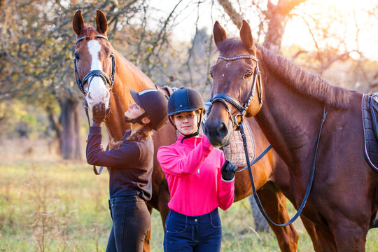 Two teenage girls with their horses in autumn park. Equestrian sport background with copy space