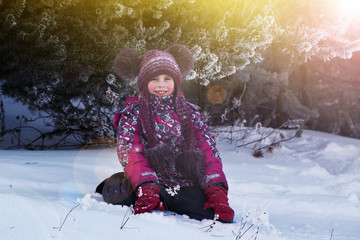 Baby girl sits at snowfall. Child in winter clothes playing with snow.