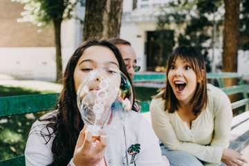 Sweet little girl playing with her father and sister while making soap bubbles on an autumn day outdoors. Father's day. Lifestyle
