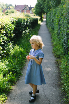 Little girl in summer school uniform stands on a path in England.