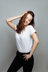 Portrait of a pretty smiling woman brunette in a white t-shirt posing isolated on a white background. the girl smiles and does up hair.