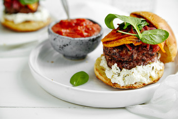 Burgers with grilled beef patties, cream cheese and spinach on classical bun. White wooden background