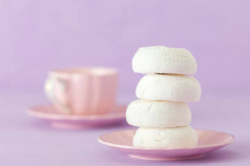 White zephyr dessrt on pink plate, cup of coffee with milk on pastel violet background. Beautiful sweets. Horizontal banner, greeting card for birthday, wedding. Close up photography. Selective focus