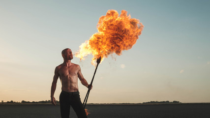 Male acrobat performing spitting fire act at the beach