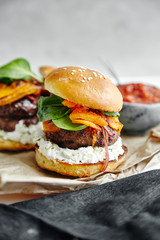Burgers with grilled beef patties, cream cheese and spinach on classical bun. White wooden background