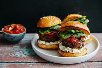 Burgers with grilled beef patties, cream cheese and spinach on classical bun. Dark rustic wooden background