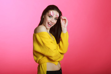 beautiful positive young girl in a yellow sweater in pink glasses on a pink background