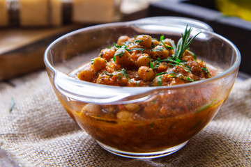 Chickpeas in tomato sauce with herbs in a glass bowl side view