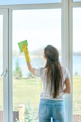 Young female wiping window. Girl working indoors. Best glass cleaner.