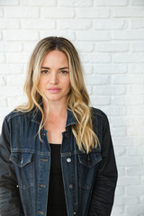 Serious looking young blonde woman in against white brick wall 