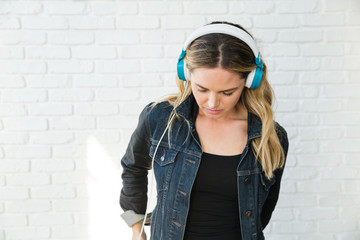 Blonde women wearing headphones and denim jacket looks down 