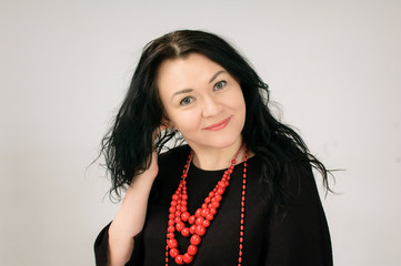 A beautiful dark-haired woman touches her hair. A large portrait. She is dressed in a black dress. She has red ethnic necklaces on her neck