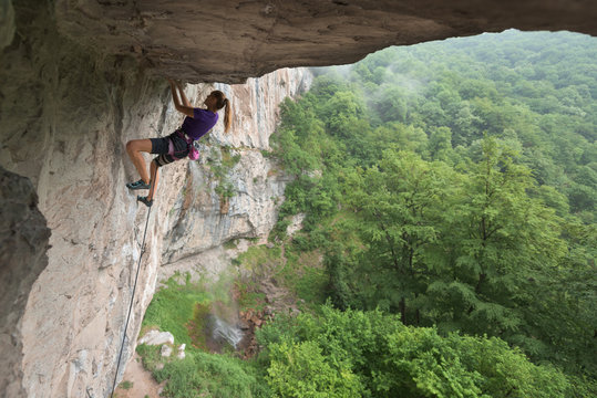 Pretty caucasian female rock climber holding on cave ceiling
