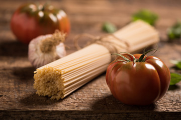 Spaghetti and tomatoes with herbs on an old and vintage wooden table. Pasta ingredients