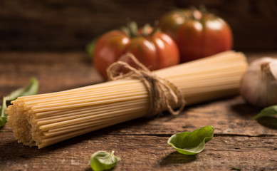 Spaghetti and tomatoes with herbs on an old and vintage wooden table. Pasta ingredients