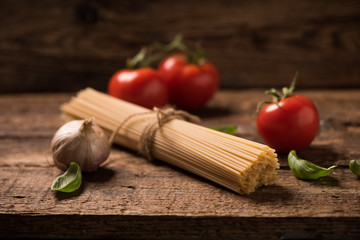 Spaghetti and tomatoes with herbs on an old and vintage wooden table. Pasta ingredients