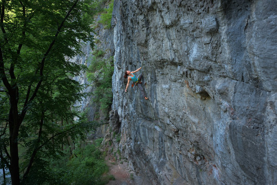 Female rock climber hanging in one arm of steep craggy wall