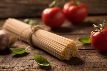 Spaghetti and tomatoes with herbs on an old and vintage wooden table. Pasta ingredients