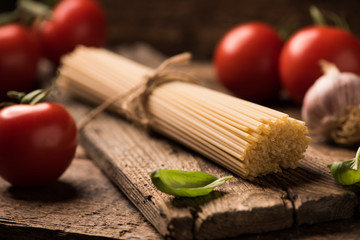 Spaghetti and tomatoes with herbs on an old and vintage wooden table. Pasta ingredients