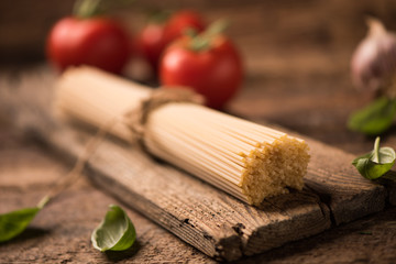 Spaghetti and tomatoes with herbs on an old and vintage wooden table. Pasta ingredients