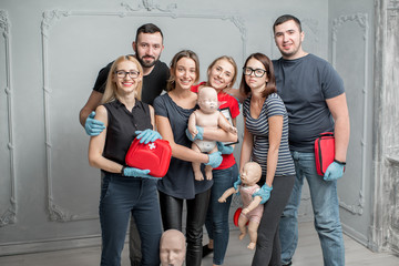 A group photo of a young people standing together and holding dummies and emergency kits after the first aid training indoors