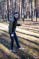 A young man of criminal appearance in a black leather jacket posing in an autumn forest.