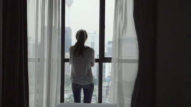 Attractive young woman alone with her thoughts standing by the window at home.