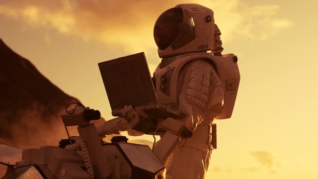 Astronaut in the Space Suit Works on Laptop, Adjusting Rover For Mars further Mars Exploration.Space Exploration Concept.First Manned Mission on Red Planet. Shot on RED EPIC-W 8K Helium Cinema Camera.